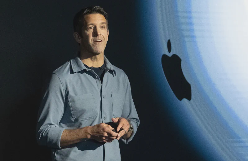John Ternus, Senior Vice President of Hardware Engineering, presenting at an Apple event against an Apple logo backdrop